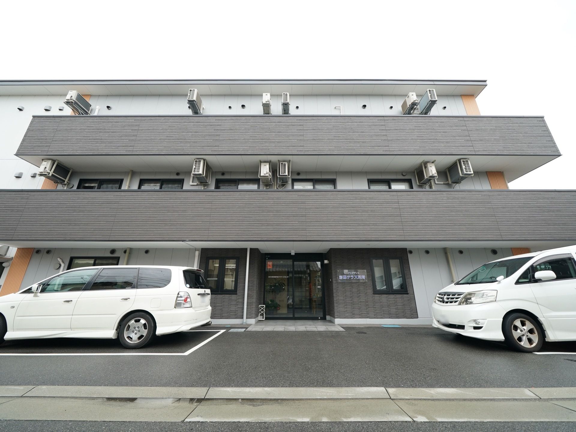 施設は３階建ての建物で、道路から玄関までは段差がない。玄関前にはひさしがついていて、傘立てが置かれている。