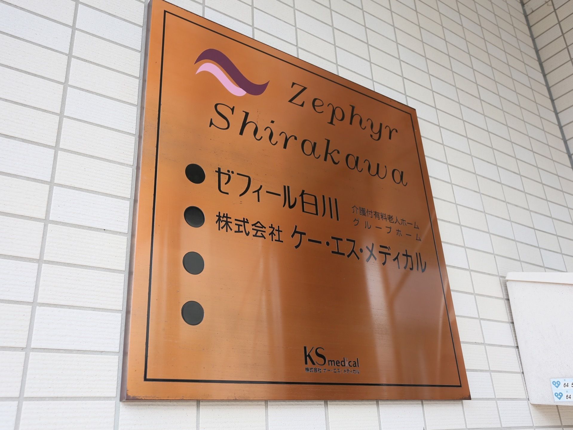 施設の壁には四角い茶色のプレートが掲げられている。施設の名前とその種類について英字と日本語で記されている。