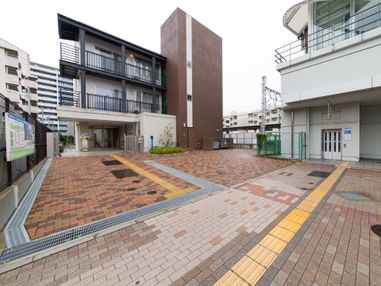 施設の入口に向かう道には点字ブロックがある。建物は３階建てになっており、入口の周辺では植物を栽培している。