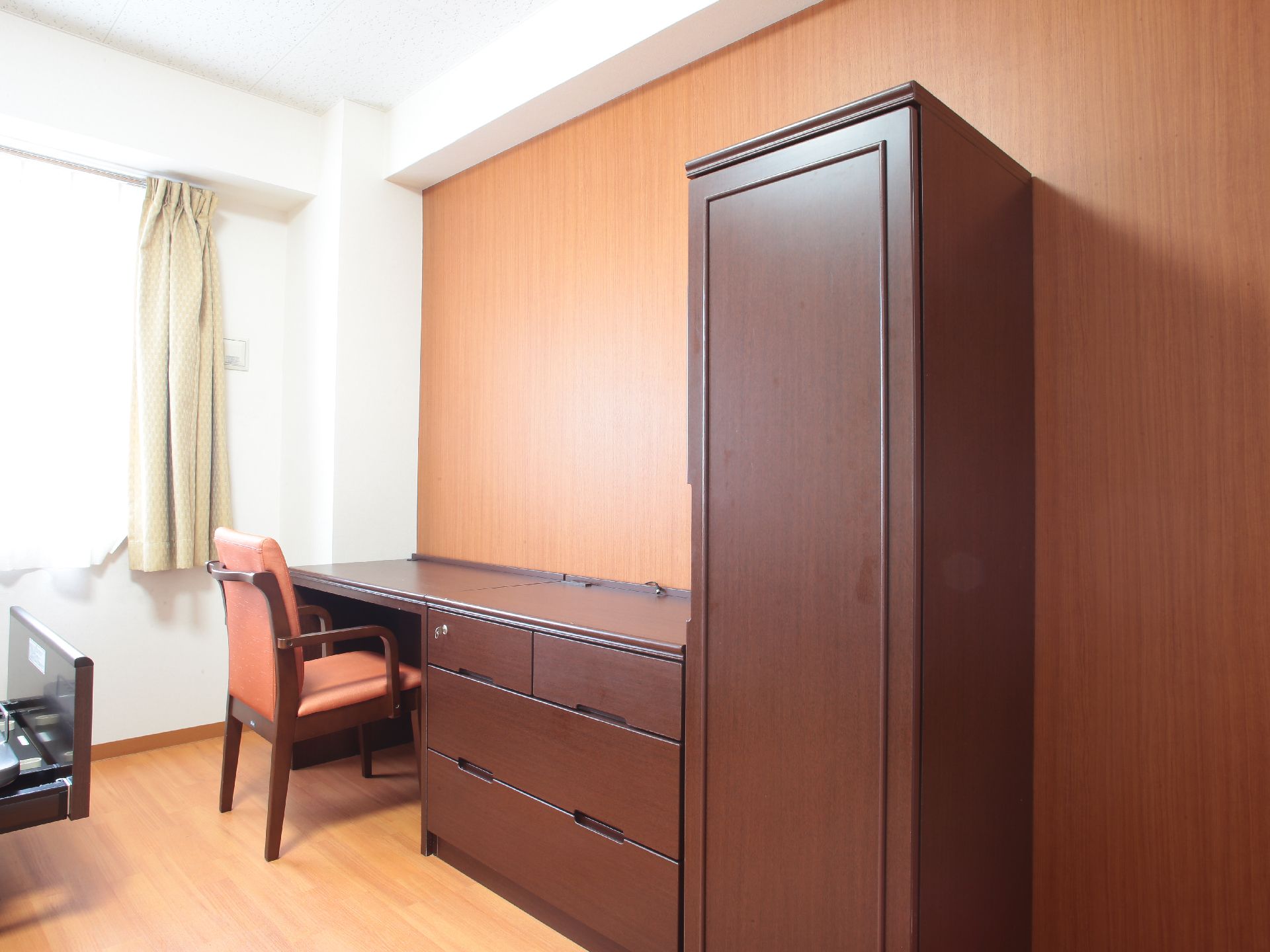 黄色のカーテンが取り付けてある腰高窓がある。部屋の床はフローリングになっている。茶色の鍵付きの机がある。