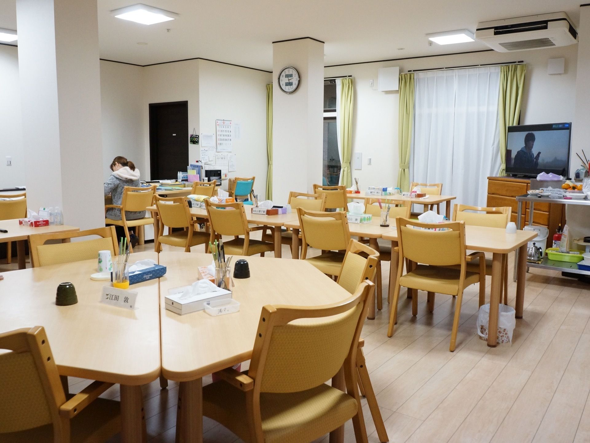 食堂にはレースと黄緑色のカーテンが掛かっている。正方形や台形のテーブルの上にはテッシュボックスや箸立てに入った箸、湯飲みが置かれている。