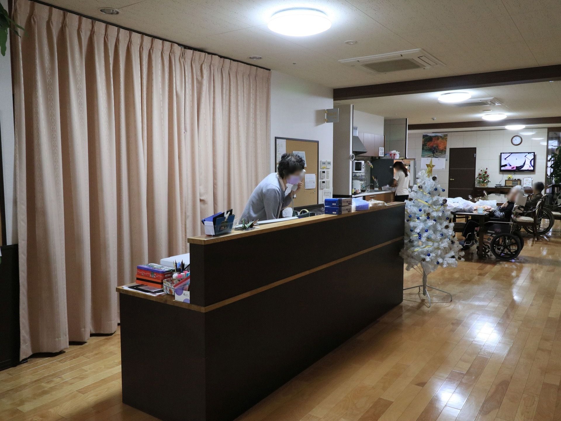 台所が併設された共有スペースが隣にある。スタッフが電話対応をしている。クリスマスツリーが飾られている。