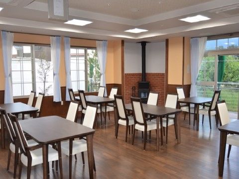 窓が大きくとられ、外には緑が広がっている。室内の隅にはストーブが設置され、複数のダイニングセットが置かれている。