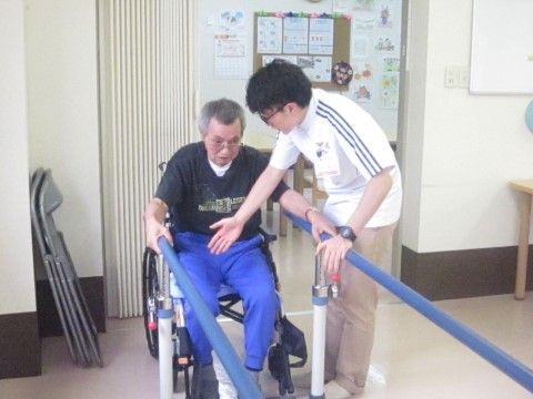 平行棒を使ってリハビリをする男性とサポートするスタッフ