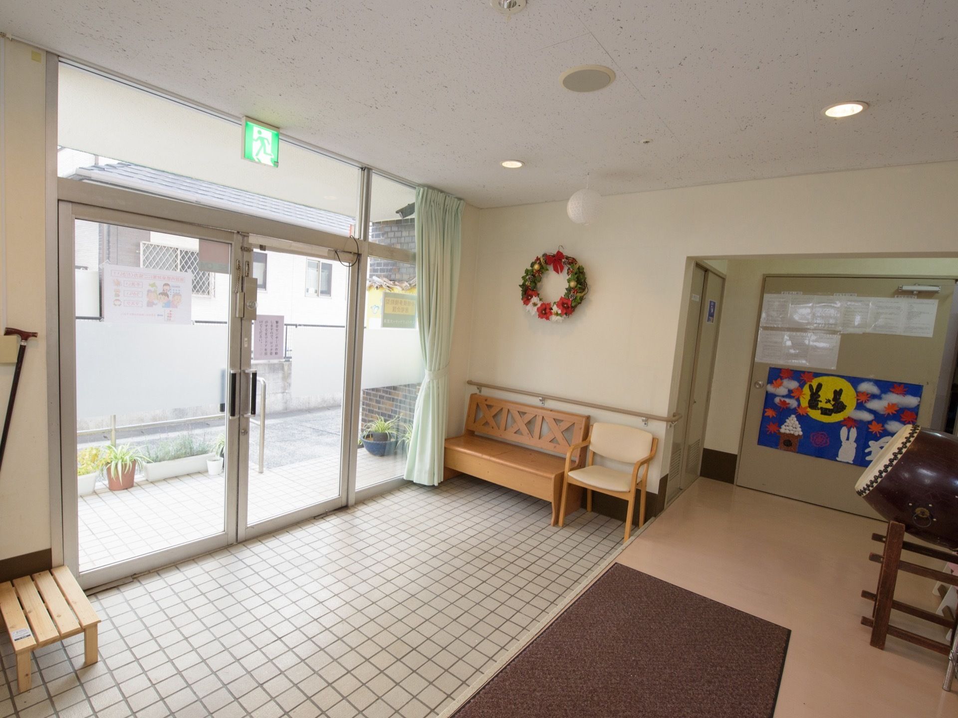 玄関ホールには、太鼓やクリスマスリースに入居者様の作品を飾っている。玄関には１段の段差があり、敷物が敷かれている。