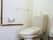 茶色い木目調の床のトイレがある。壁には縦横方面に手すりが設置されている。タオルハンガーがあり、側にはごみ箱が置かれている。