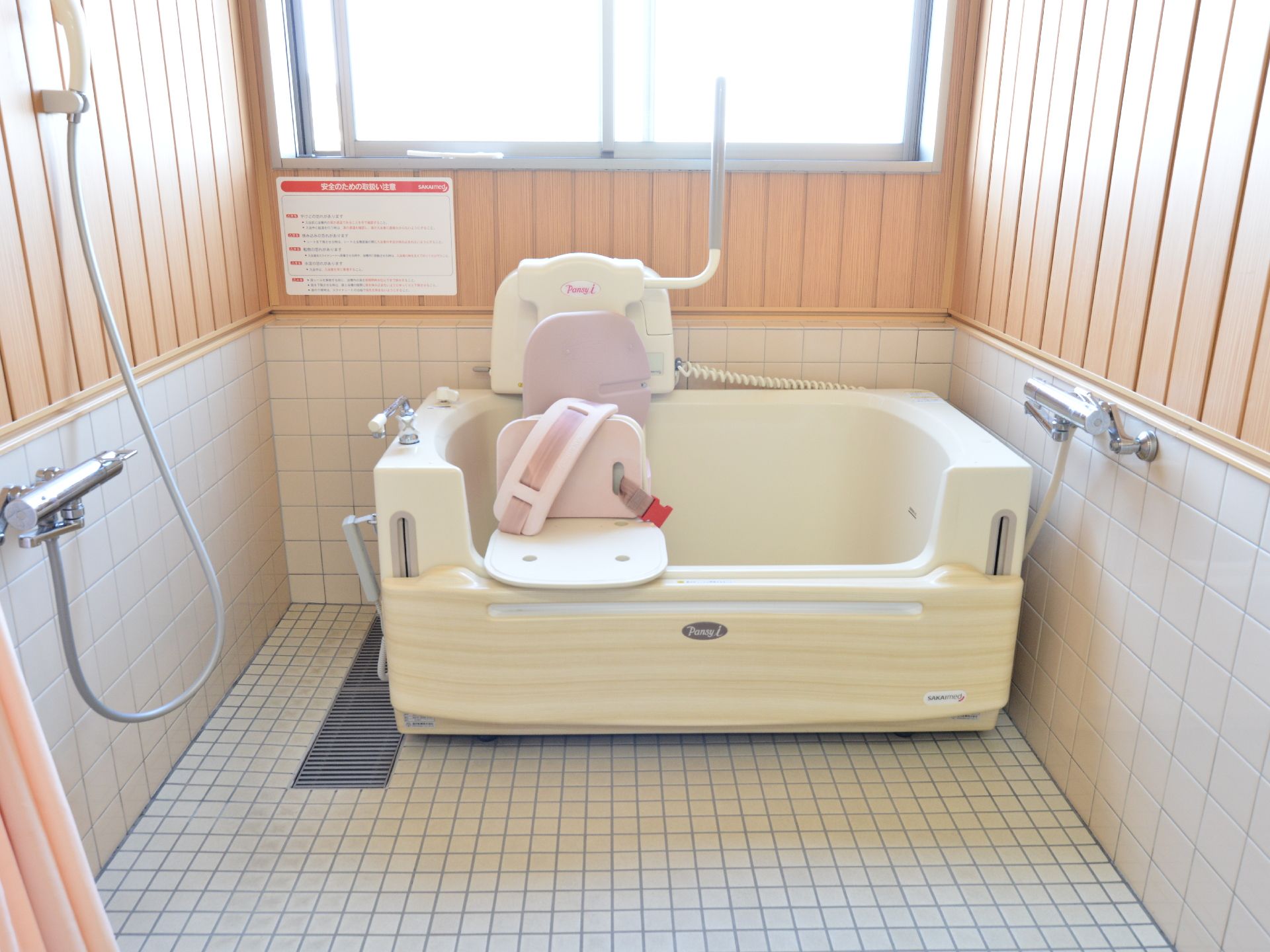 昇降ユニットが浴槽に装備されている。床は濡れても滑りにくいタイル式の床になっている。壁には緊急呼び出しボタンが設置してある。