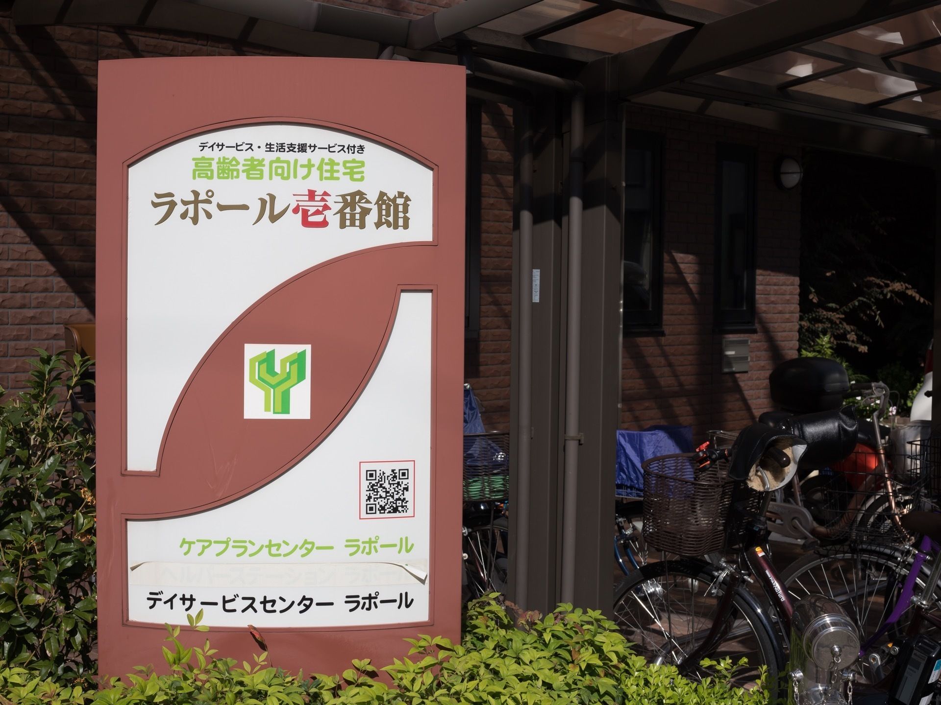 正面玄関横には施設の看板が立てられている。高齢者向け住宅以外に、デイサービスも利用できる旨が紹介されている。