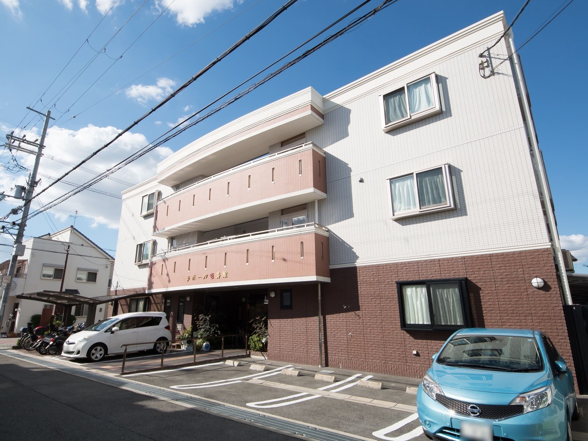 正面玄関側から見た施設外観。中央のバルコニー風の張り出しは、ややカーブを描いてふくらんでおり、施設名のロゴが入っている。