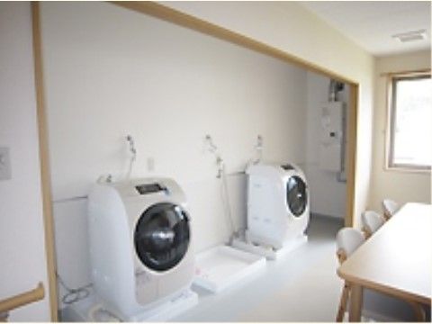 ドラム式の洗濯機を２台設置した部屋には、テーブルセットがあり、おしゃべりをしながら洗濯が終わるのを待てる。