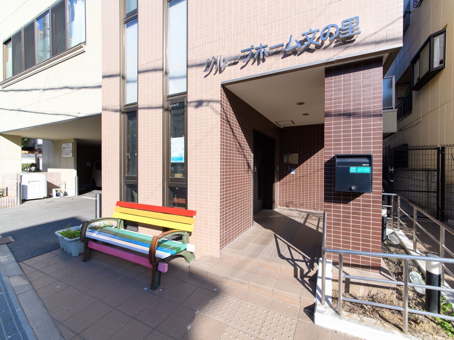 壁の色は茶色で、入口の上には大きくグループ名の表記がされている。入口横にはカラフルなベンチが設置されている。
