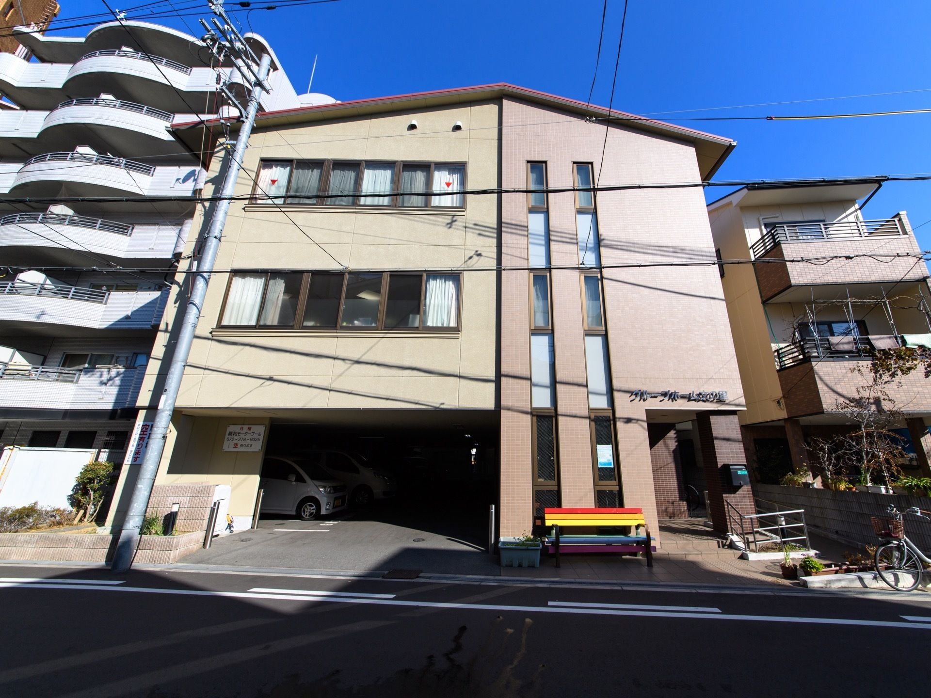 ３階建ての建物で、壁の色は茶色である。１階は玄関と駐車場になっている。道路に面してベンチが置かれいる。