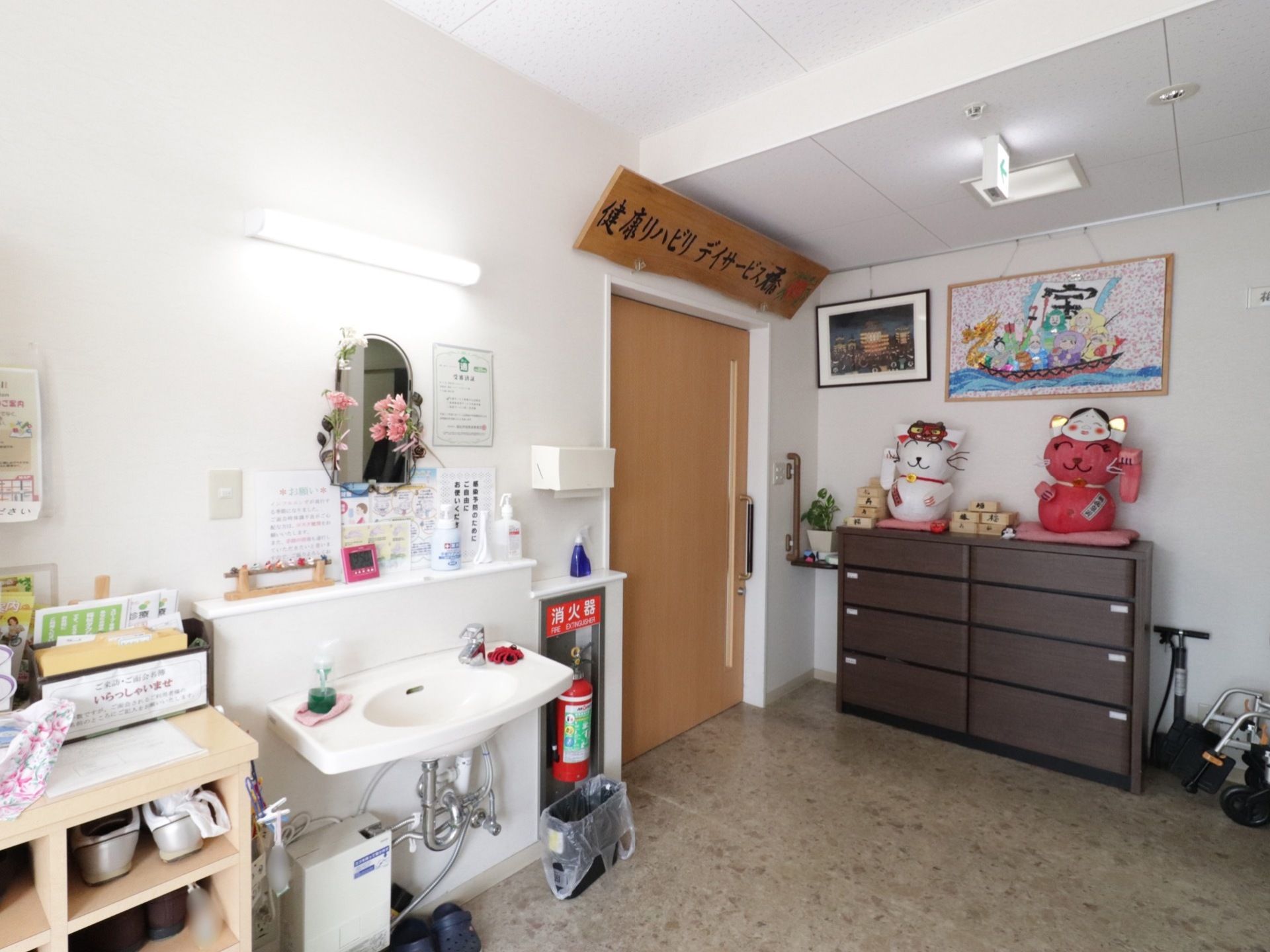 玄関に入ってすぐの場所に、靴が入れられた靴箱が置かれている。近くには洗面台がある。壁には2枚の絵が飾られている。