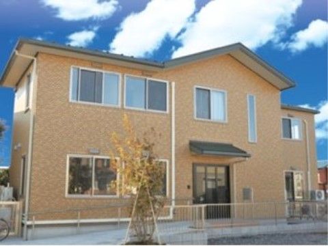 目の前に高い木が植えられている、入り口までスロープが続く二階建ての建物