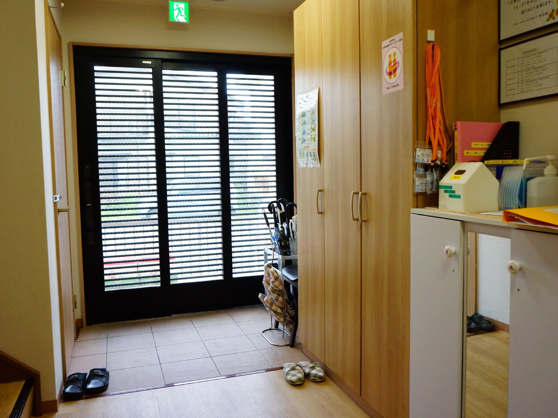 黒い3枚の扉が玄関になっており屋内へはバリアフリーで繋がっている。右手に木製の棚があり左手には階段が見える。