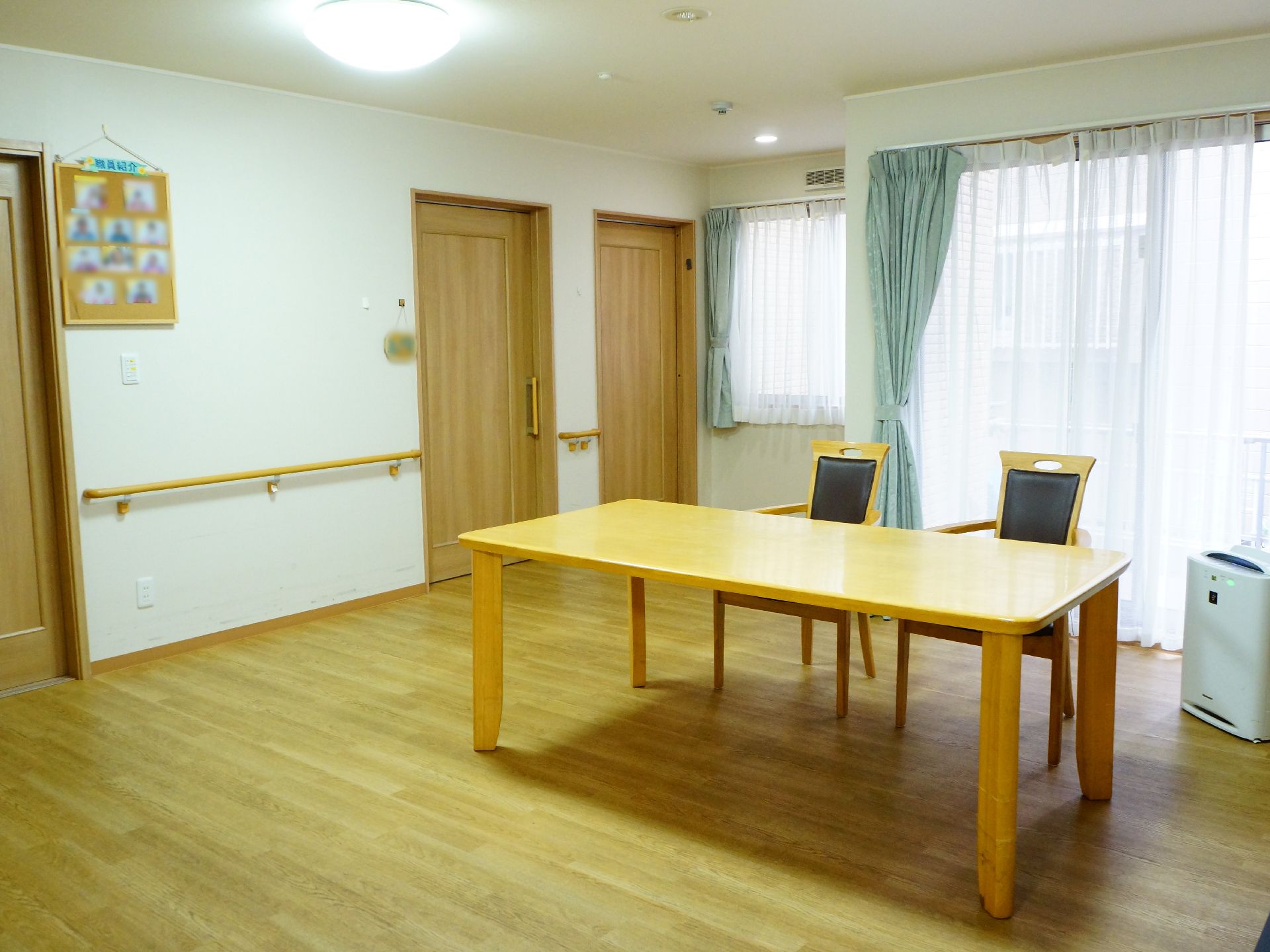 フローリングの部屋に窓から淡い光が差し込んでおり、天井からも照明が灯っている。木目調のテーブルと椅子も用意されている。