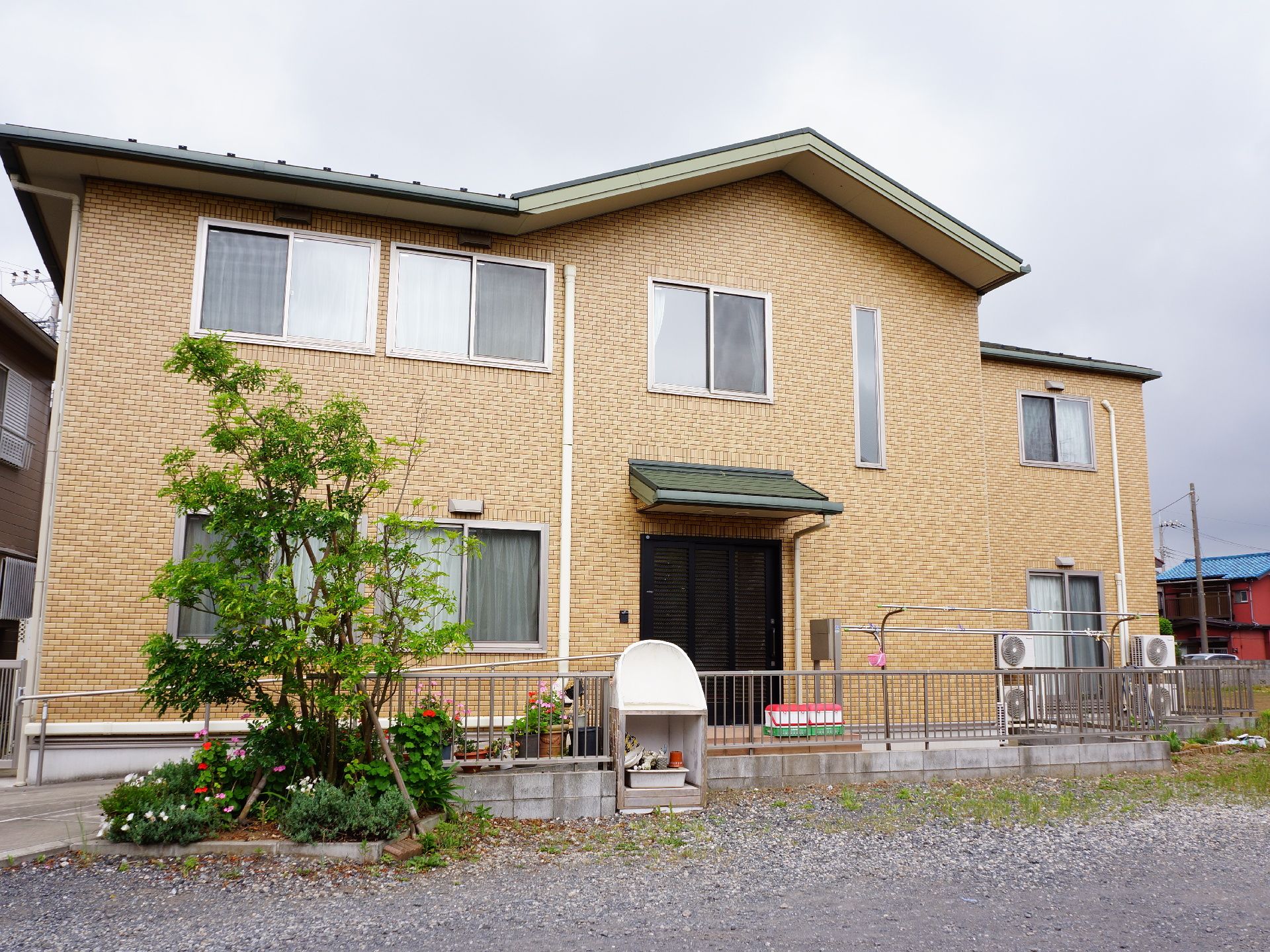 2階建の茶色の外壁の施設になっている。フェンスに囲まれ手前には樹木が植えてあり、左手からスロープがのびている。
