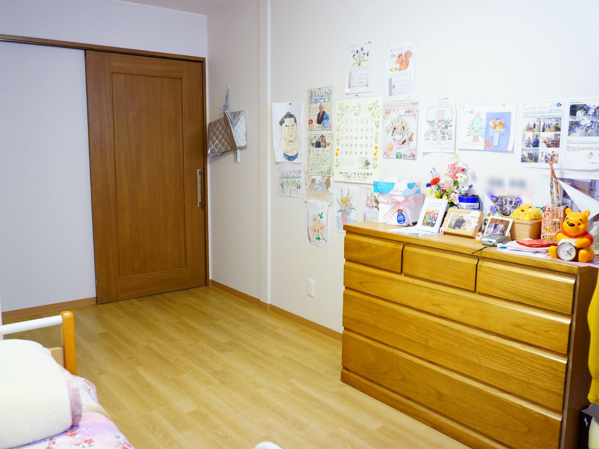 スライド式のドアが入り口になっており、右手の壁にはいろいろな張り紙がしてある。木目調のタンスが手前には置かれている。