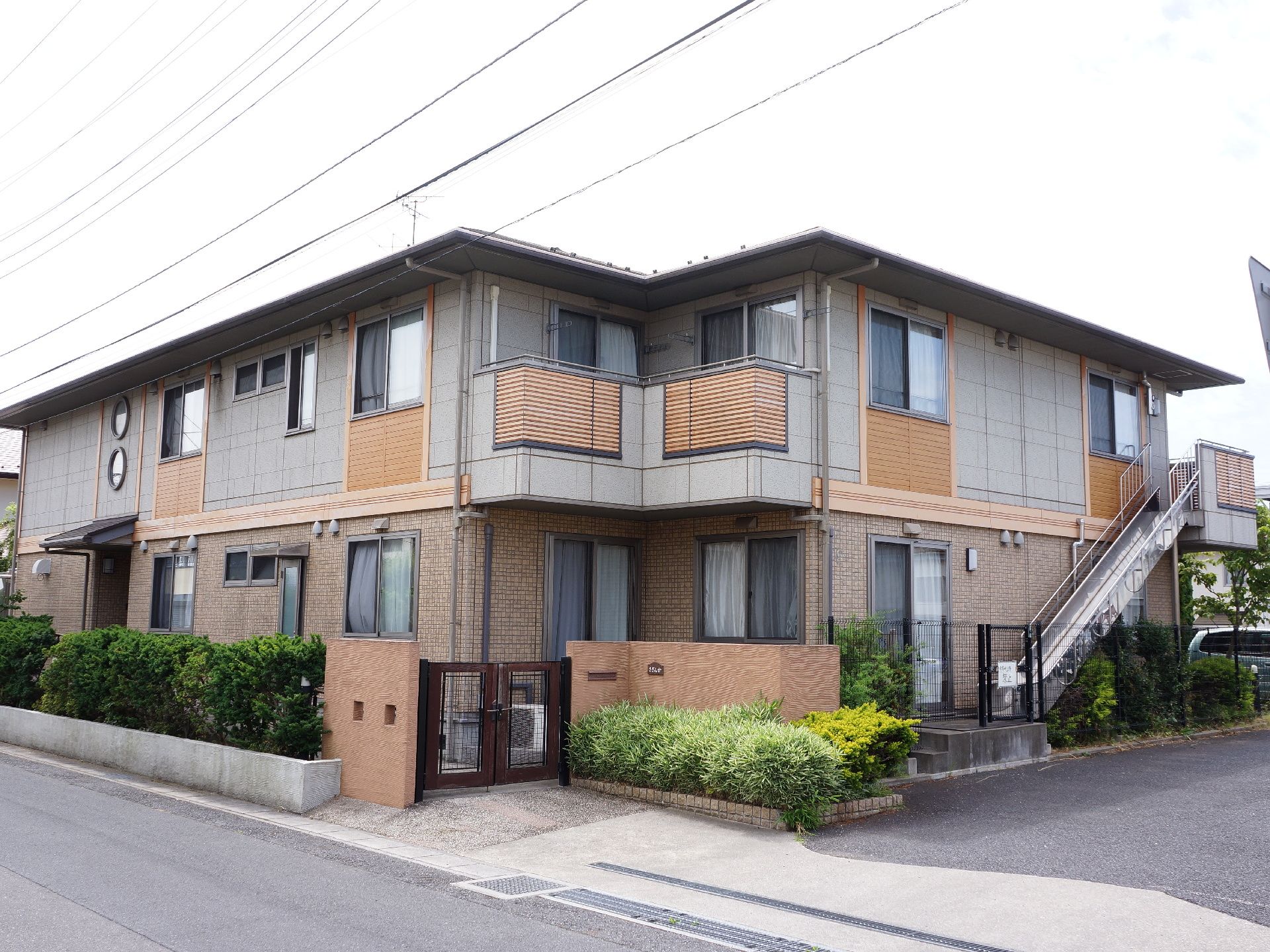 2階建てのグレーとブラウンでデザインされた施設になっている。右側に外階段がついており道路に面して建っている。