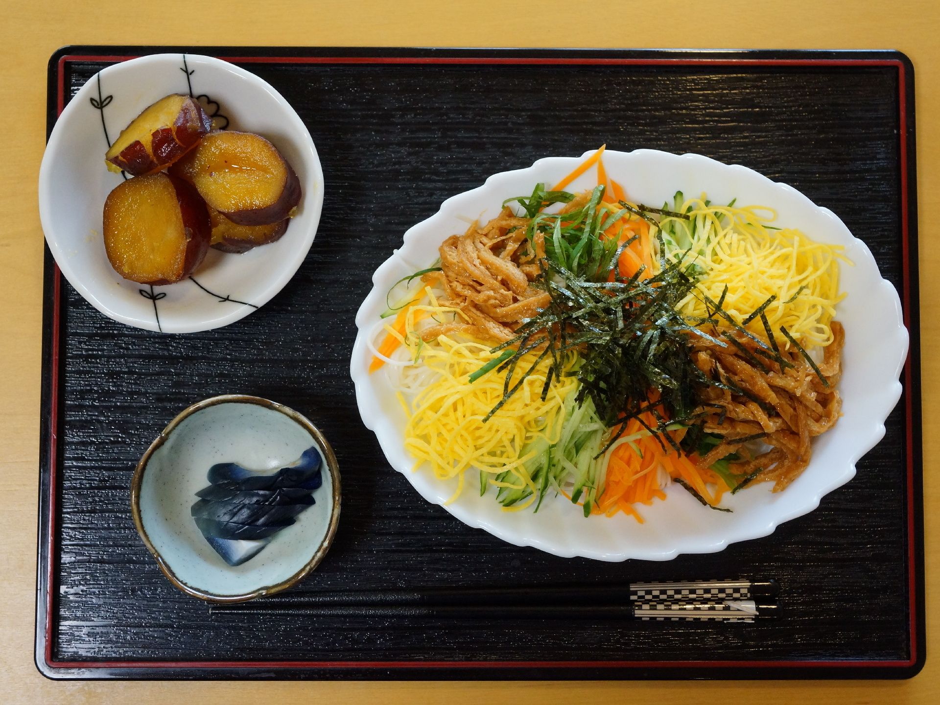 黒いトレーの上に、箸と食事が載せられている。この日はちらし寿司と漬物、サツマイモ煮のメニューである。
