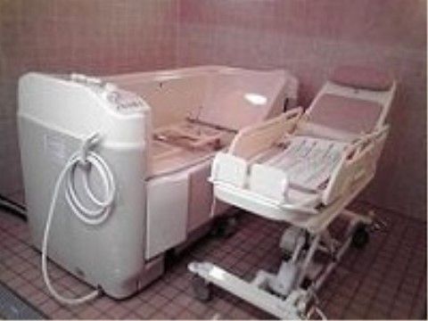 白とピンクを基調とした浴室は、お洒落なイメージである。寝たままの状態で湯船に浸かれる機械浴を備えている。