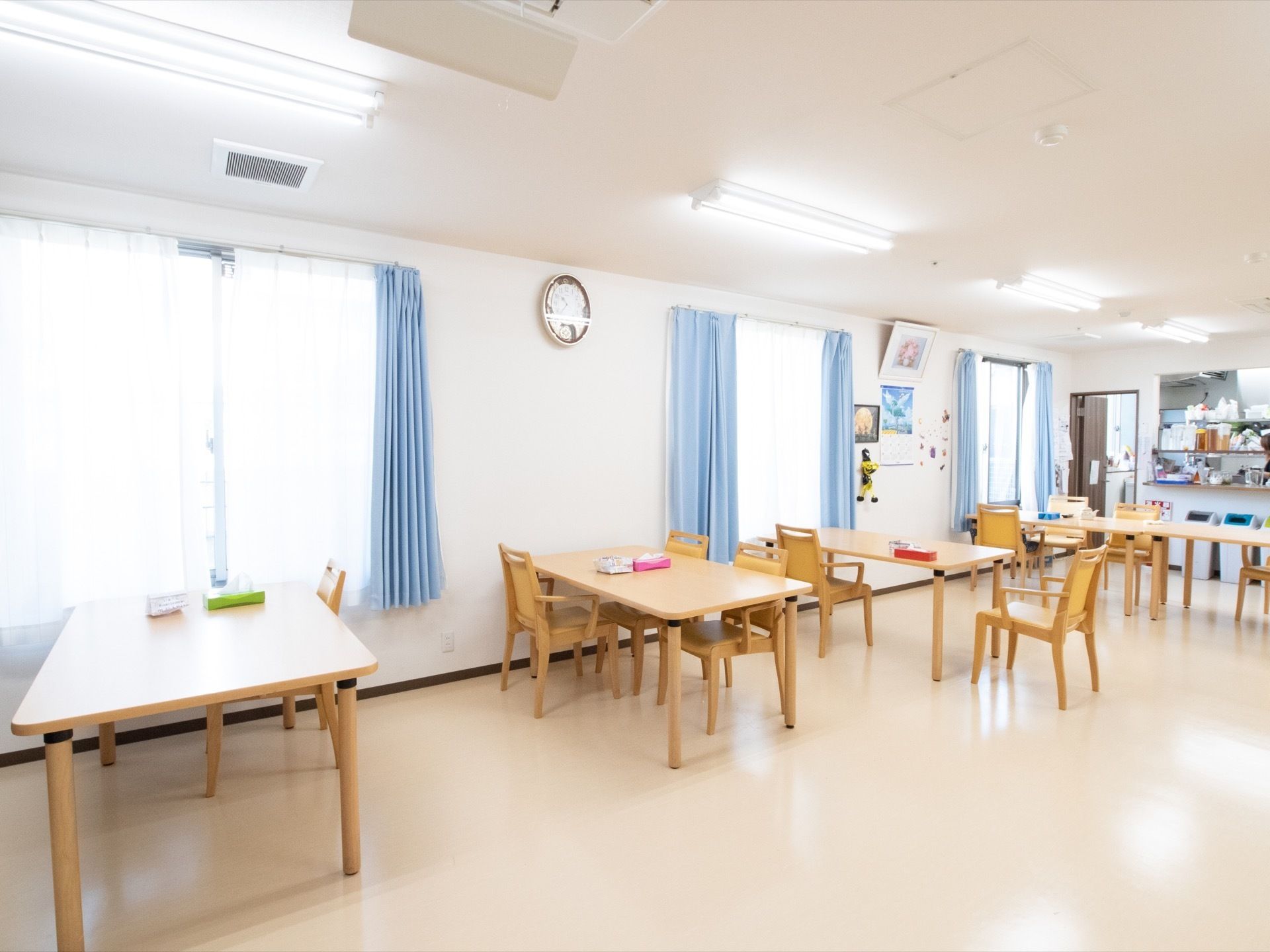 食堂にはたくさんの窓が取りつけられており、テーブルや椅子が並べられている。壁には、時計が掛けられている。