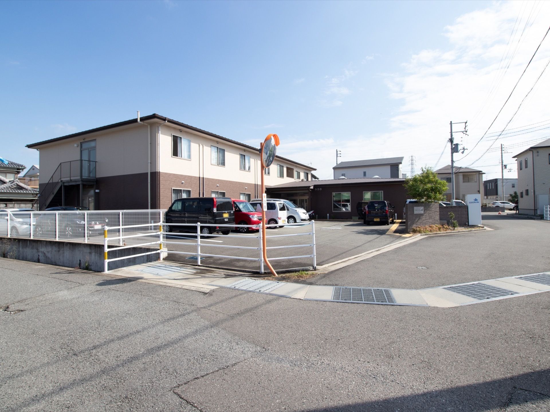 施設は２階建てで、敷地内には広い駐車スペースが設けられている。左側には、２階へ繋がる屋外階段が設置されている。