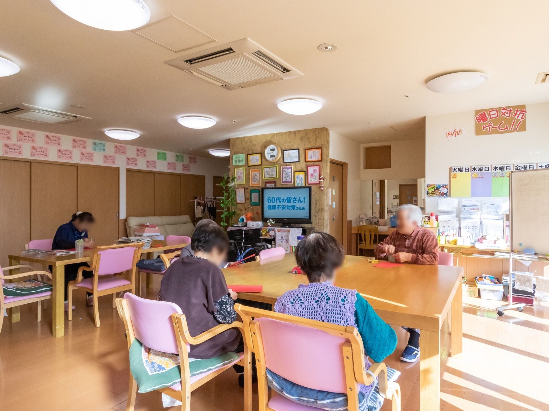 天井にたくさんの照明が設置されているリビングである。入居者様がテーブルを囲んで、工作を楽しんでいる。