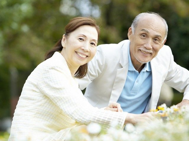 ご高齢の男女がお花畑のなかで微笑んでいる様子。