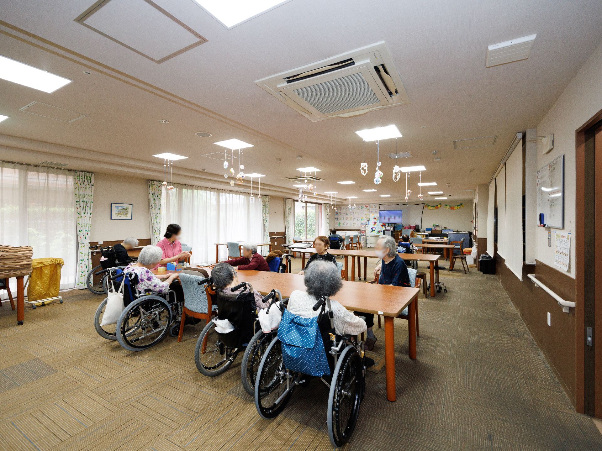 入居者様が周りに座る木製の机が置かれた白い壁の部屋