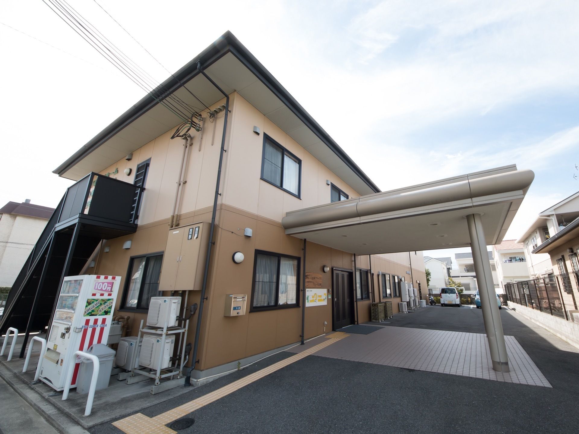 道路側から施設の入り口まで点字ブロックが設置されている。路面は平坦で、アスファルトで舗装されている。