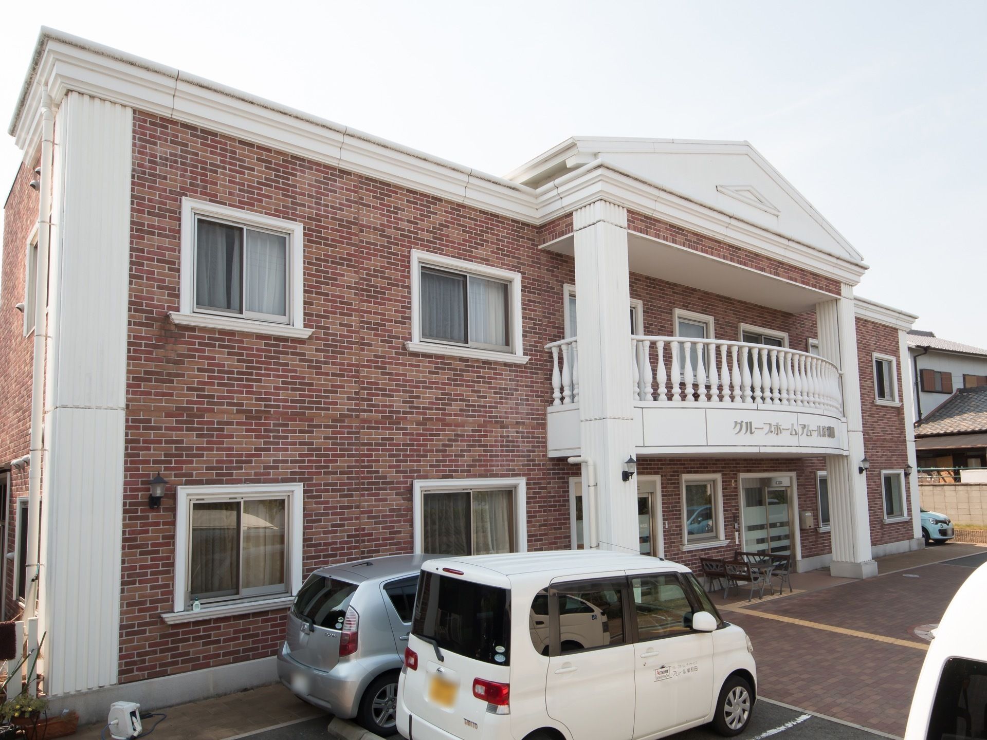 レンガ調の外壁が特徴的な２階建ての建物である。建物正面の２階部分に大きなテラスが設けられている。駐車場が完備されている。