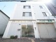 白い３階建てのビルである。施設の玄関は向かって左端である。自動ドアの横に外灯と郵便受けが設置されている。隣には薬局がある。