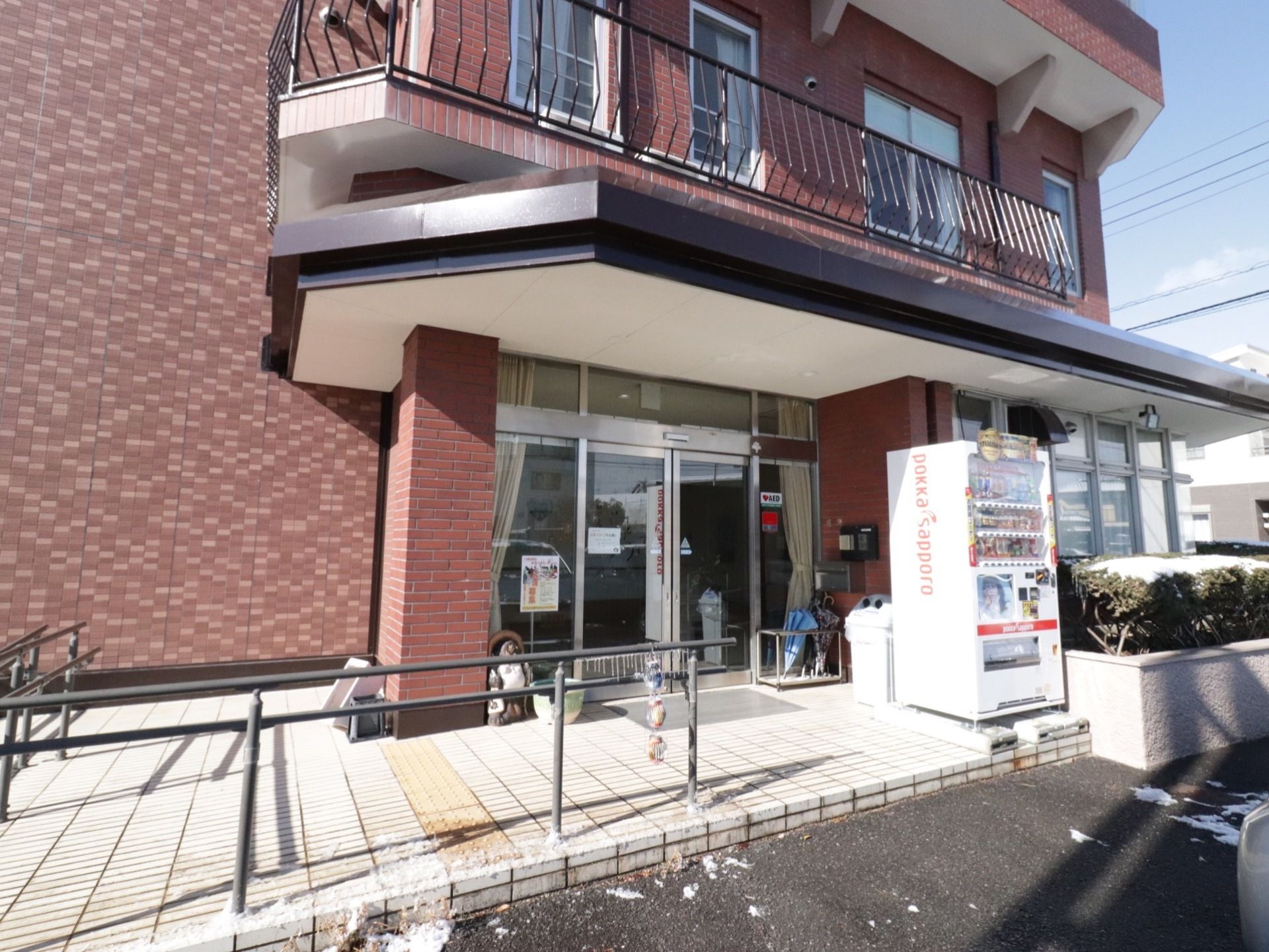レンガ調造りの施設はガラスサッシ戸の自動扉となっている。自販機が右側にあり左側にはパイプ柵が設置されている。２階にはベランダがある。
