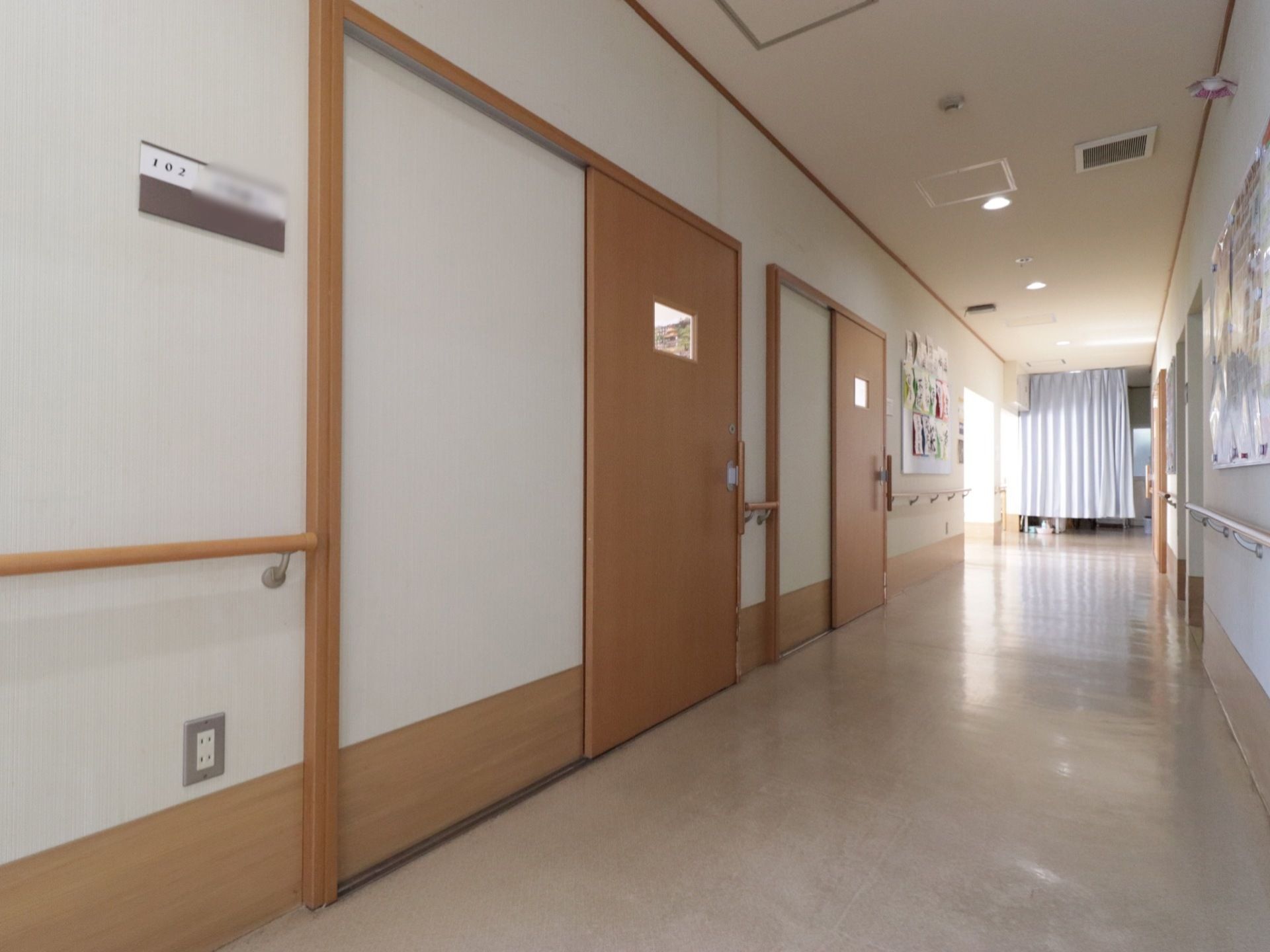 廊下の壁にはレクリエーションで作った作品等を貼っている。入居者様のネームプレートが貼られており木製の居室の引き戸には様子を伺える小窓がある。