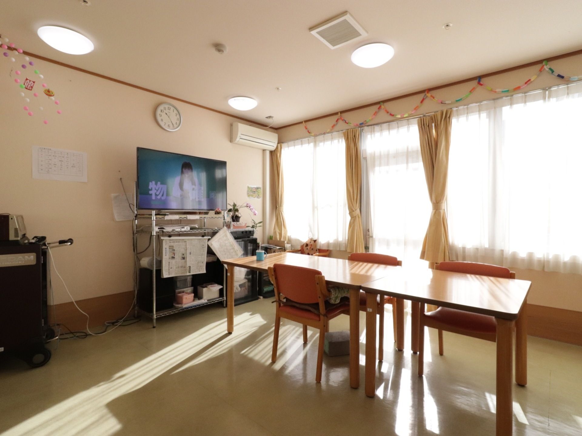 テレビと時計が設置され机と椅子が複数置かれている。壁にはリクリエーションで作ったものがかざられている。