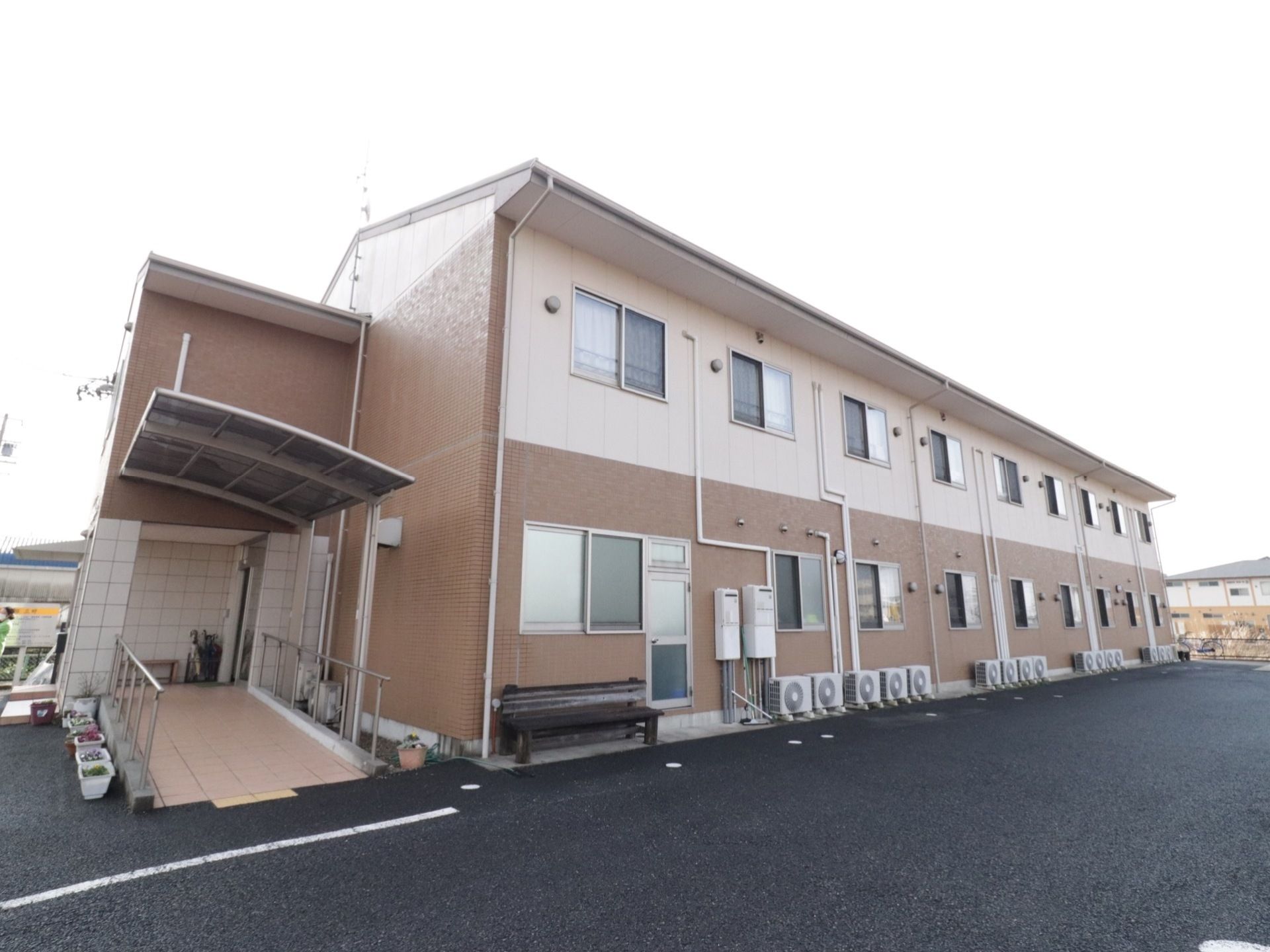 鉄骨造２階建ての施設である。エントランスに設けられているスロープには、ひさしが設置されている。ベンチが置かれている。