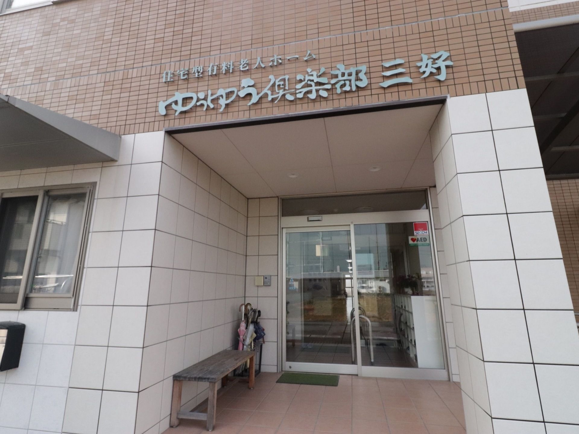 ひさし付きのエントランスである。壁際には、傘立てやベンチが置かれている。玄関は、自動ドアになっている。