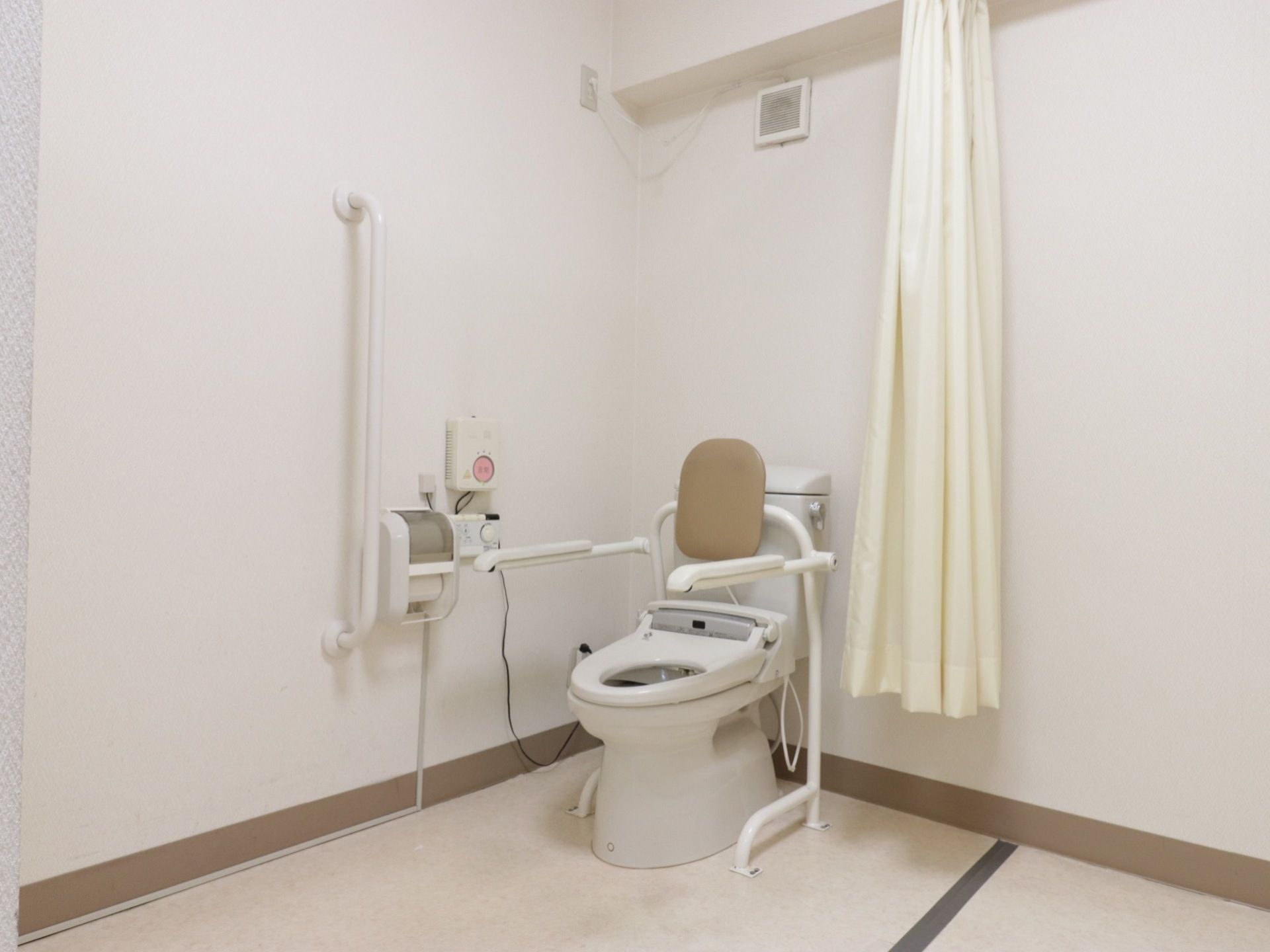 ひじ掛けと背あてが追加された洋式トイレが設置されている。広い空間を天井に取り付けたカーテンで仕切ることができる。