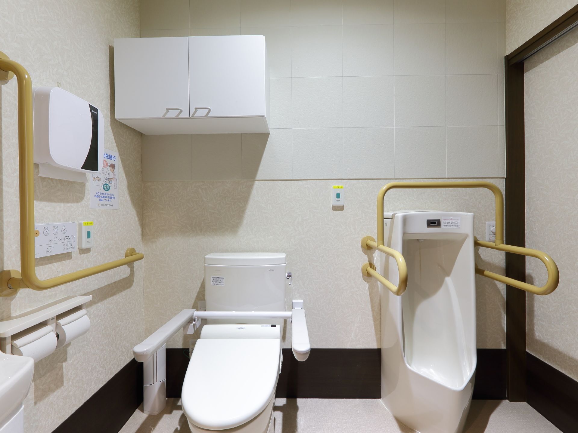 白い壁と床が印象的なトイレは、タンク付きと男性用の2種類のトイレが設置されている。タンク付きトイレの上には収納棚も取りつけられている。