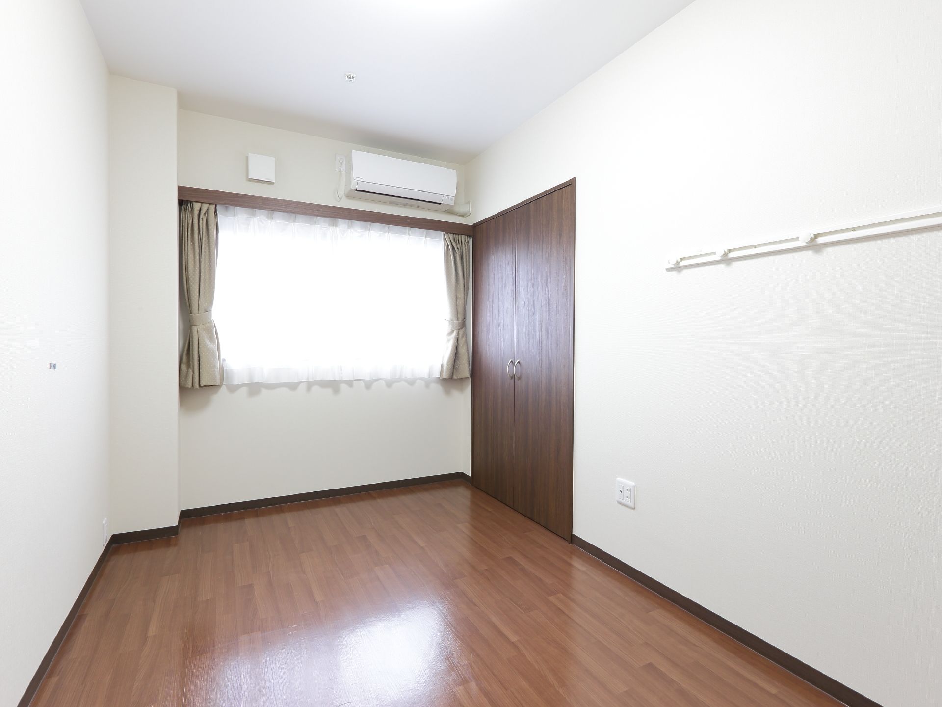 白い壁とフローリングの洋間になっている。腰高窓からは光が入り明るい部屋となっている。広いクローゼットやエアコンも完備されている。