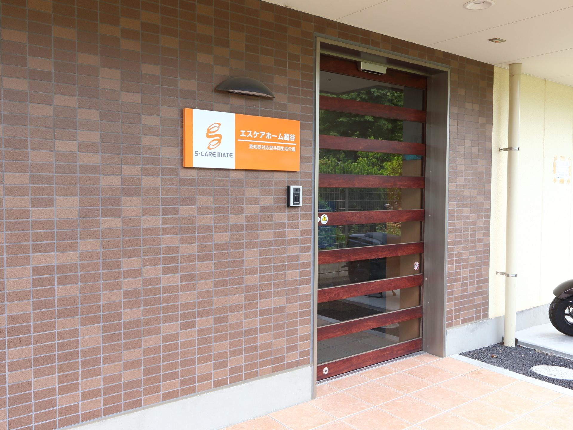 正面玄関にはオレンジの看板が目立つ。木目とガラスの自動ドアは内側からも外側からも様子が見えるので安心できる。