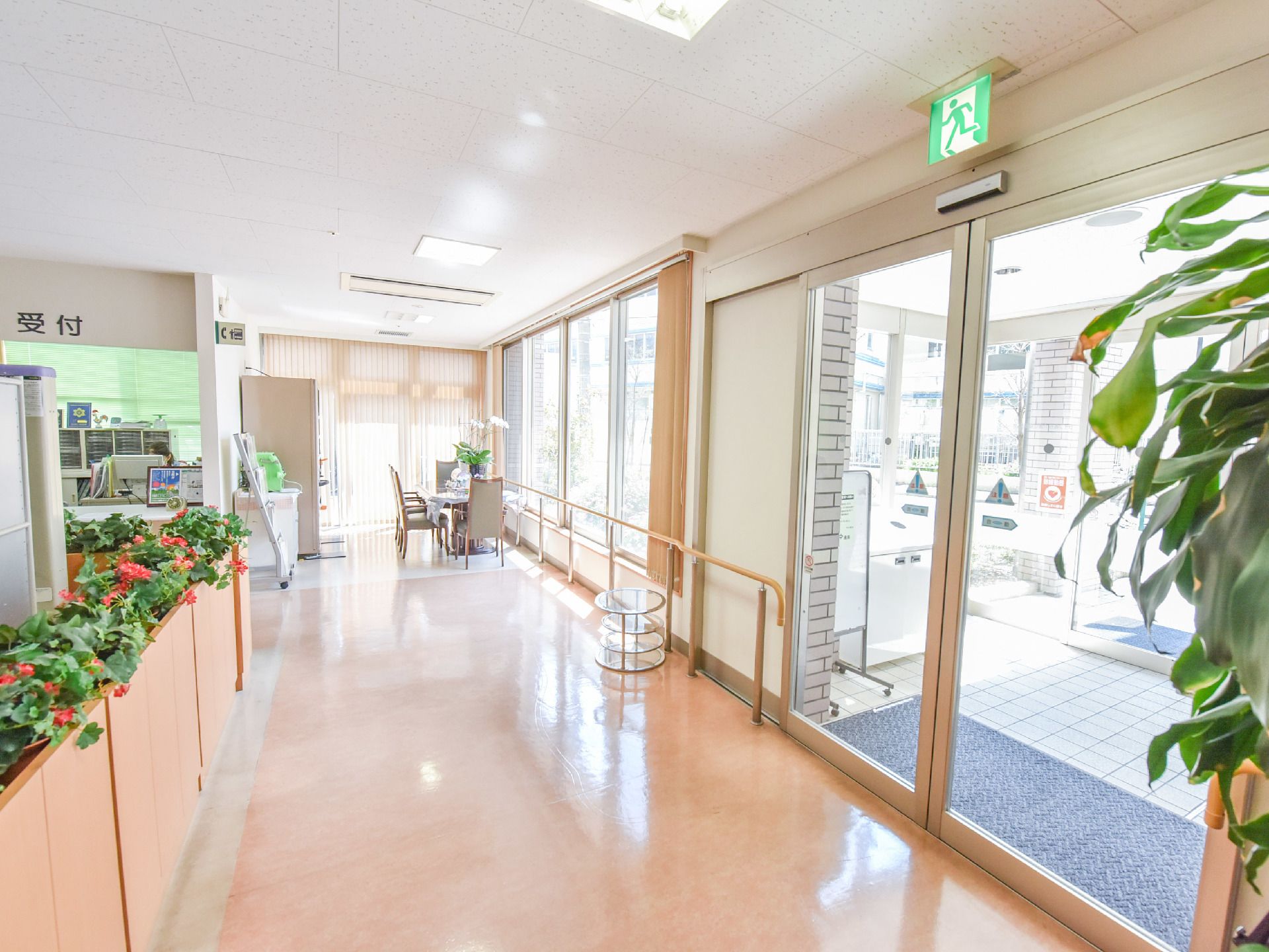 エントランス通路は広く車椅子でのすれ違いも可能な広さ。奥には受付と談話スペースが見え机と公衆電話が見える。