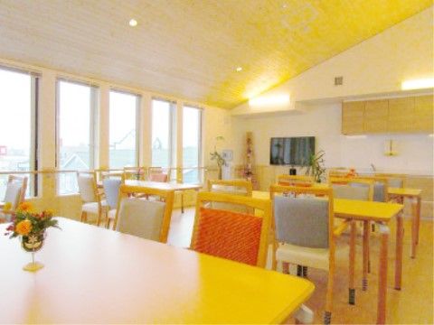 大きな窓から光が射し込む、白が基調の明るく広い部屋。４人掛けテーブルセットが等間隔で置かれ、テーブルの上には花が飾られている。