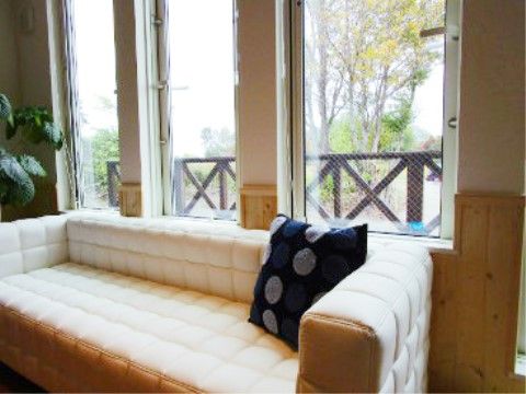 木のぬくもりがある部屋の窓辺に置かれた、大きな白いソファー。横には観葉植物がある。窓からは外の景色を見ながらゆったりできる場所だ。