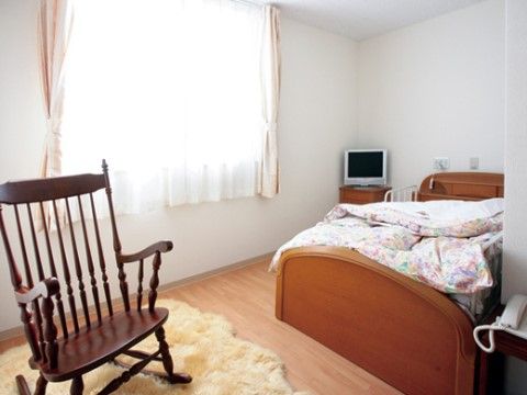 白が基調の壁で窓からの日か映え、ベッドや床は木目調で温かい色合いの部屋。連絡用の電話付きで安心して利用可能である。