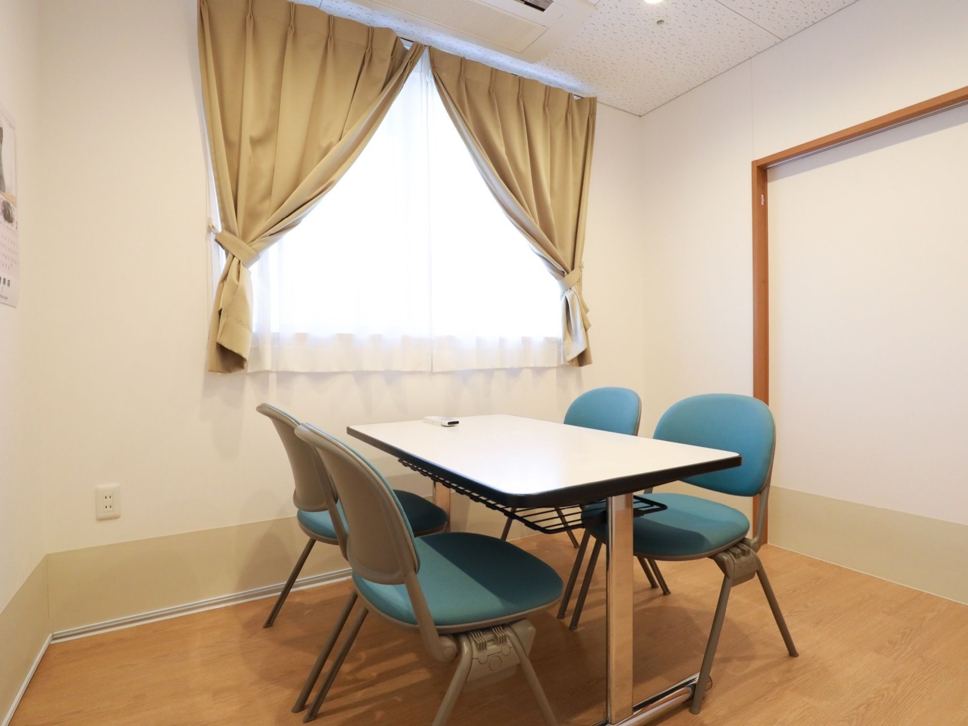 個室になった面談室。大きな窓にはカーテンが付いている。中央に4脚の椅子が配置されたテーブルが置かれている。