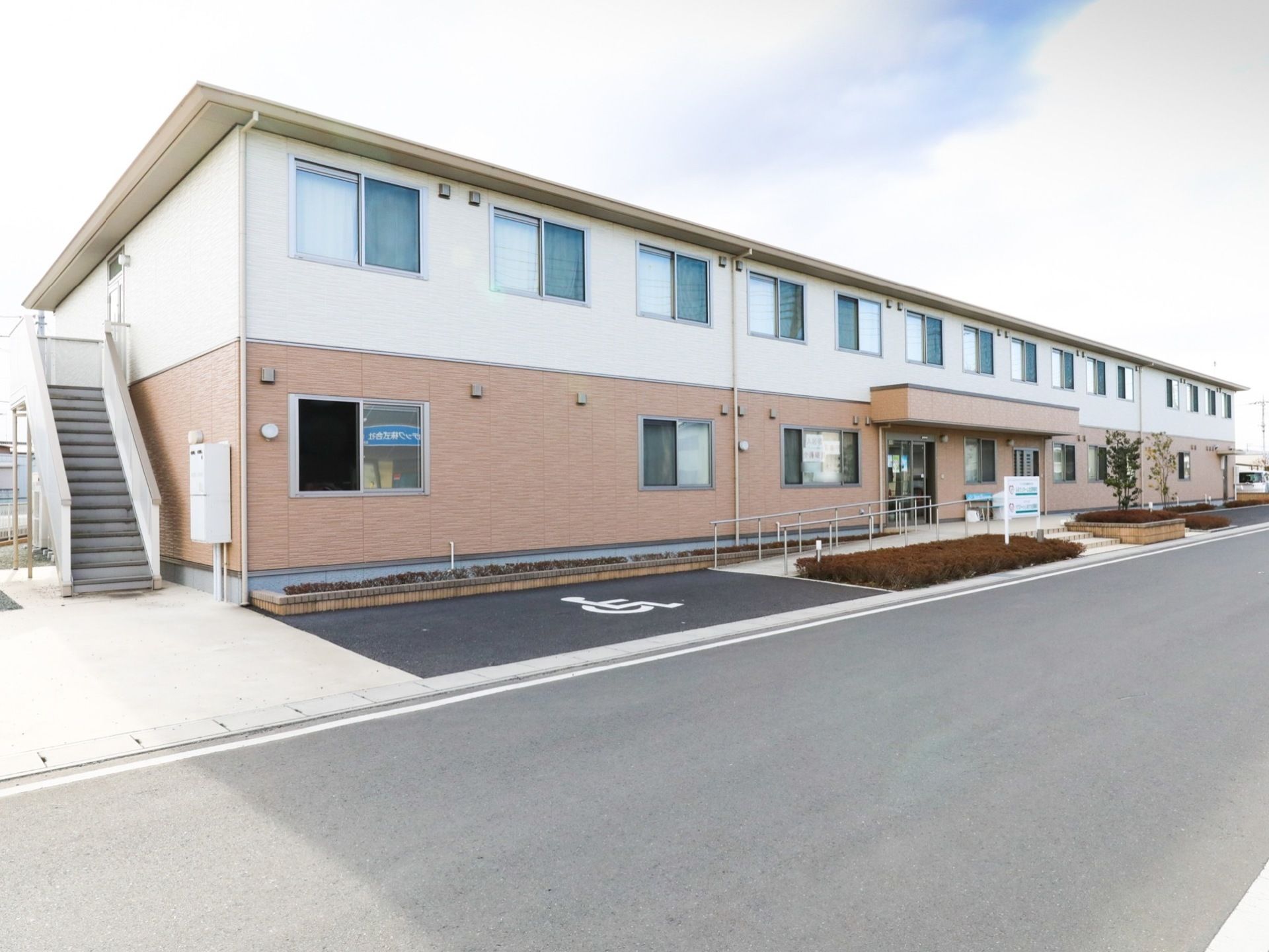 ２階建ての建物には、外階段が設置されている。エントランスには、手すりが備わったスロープや階段が設けられている。