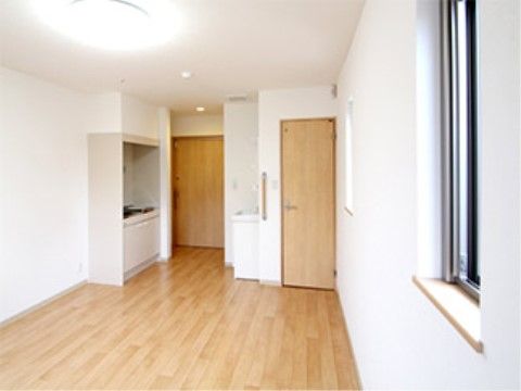 白い壁に明るい木目調の床やドアが優しい印象を与える居室。入口を入ってすぐにお湯を沸かせるミニキッチンがある。