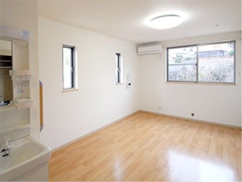 メインの窓のほか、明かりとりの窓が2つついた天然光が明るい居室。広めの室内には、収納スペースのついた洗面台が見える。